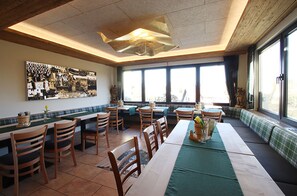 Un restaurant doté d’une longue table conviviale, de chaises en bois et d’une grande fenêtre laissant entrer la lumière naturelle.
