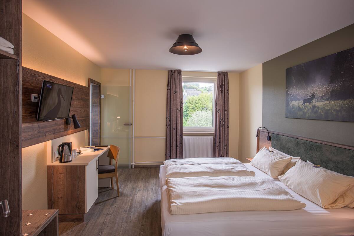 Een slaapkamer met een bed, een bureau, een stoel, een televisie en een raam met gordijnen.