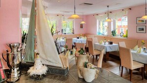 A restaurant with a nautical theme, featuring a sailboat decoration, wooden tables, and hanging pendant lights. - Seehotel Düne (Graal Mueritz)