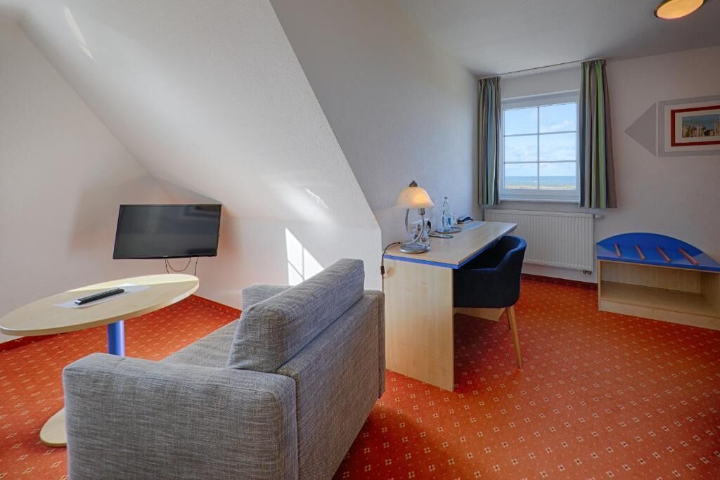 Ein kleiner, gemütlicher Raum mit einer Couch, einem Schreibtisch, einem Fernseher und einem Fenster mit Vorhängen.