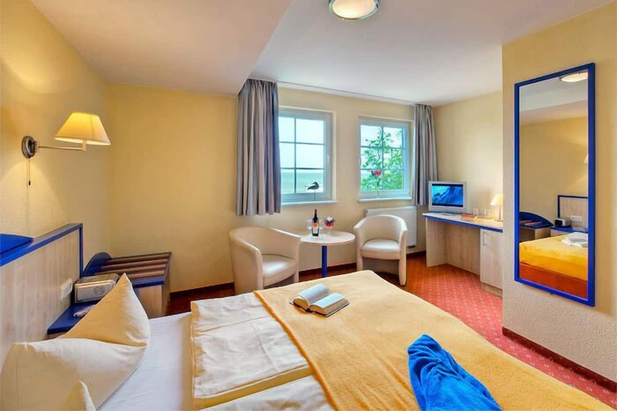 Habitación de hotel con cama, dos sillones, una mesita, televisor y ventana con cortinas.