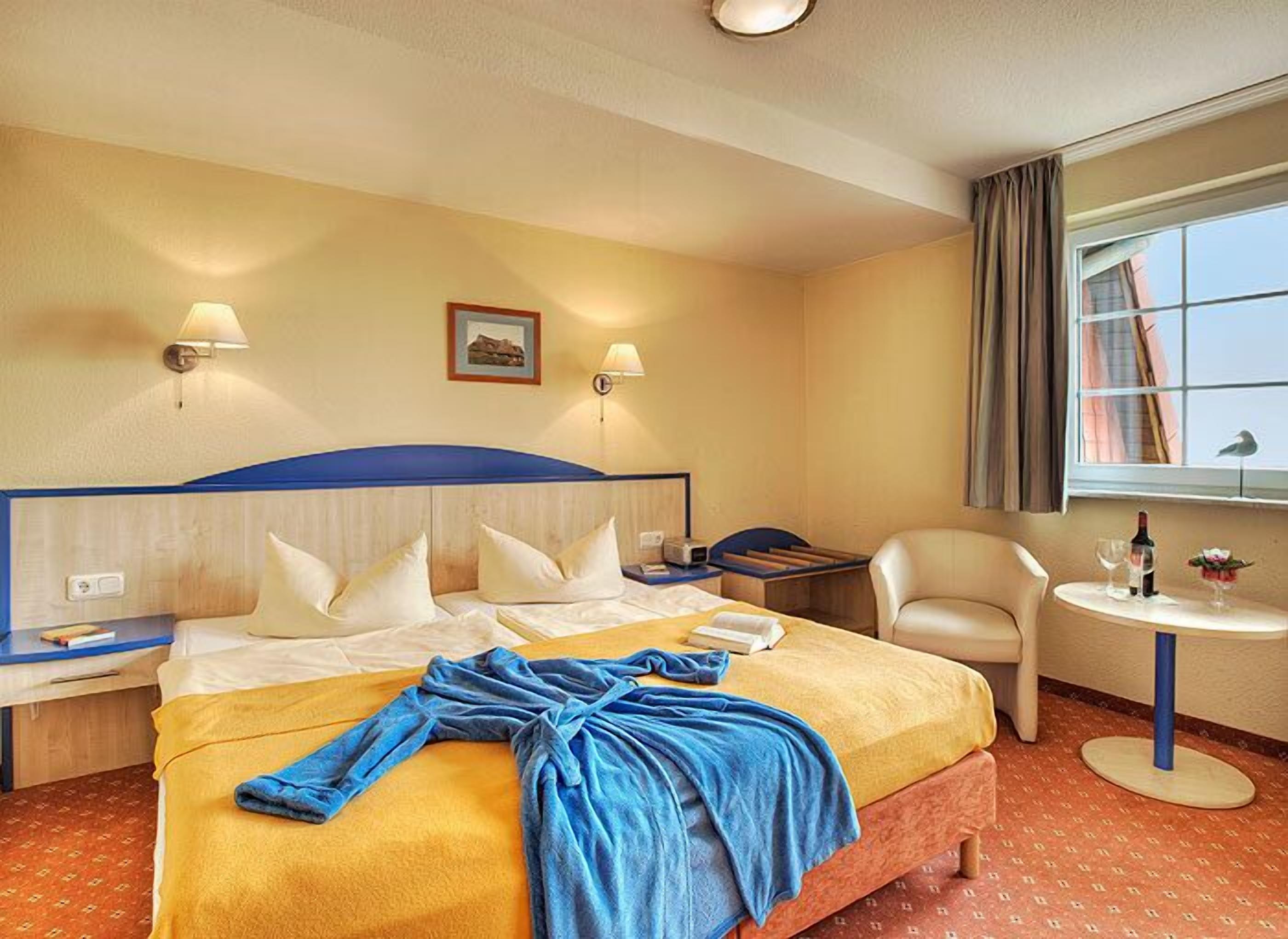 Habitación de hotel con una cama grande, dos mesitas de noche, una silla, una mesita redonda y una ventana con cortinas.