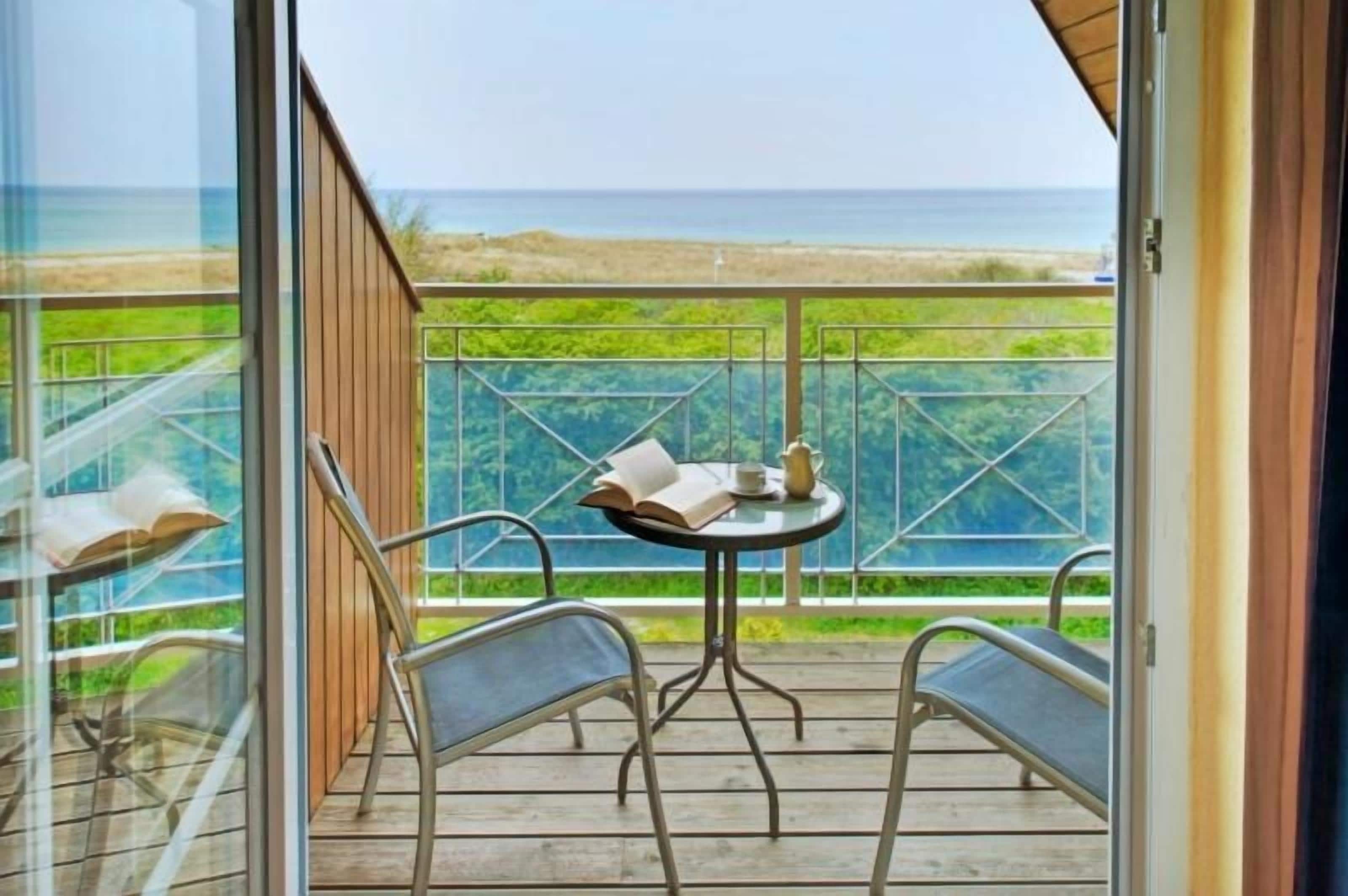 Un balcon avec une table et des chaises, une vue sur la mer et une porte vitrée.