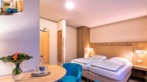 A hotel room with two beds, a desk with a vase of flowers, a bottle, and two blue chairs. - Seehotel Düne (Graal Mueritz)