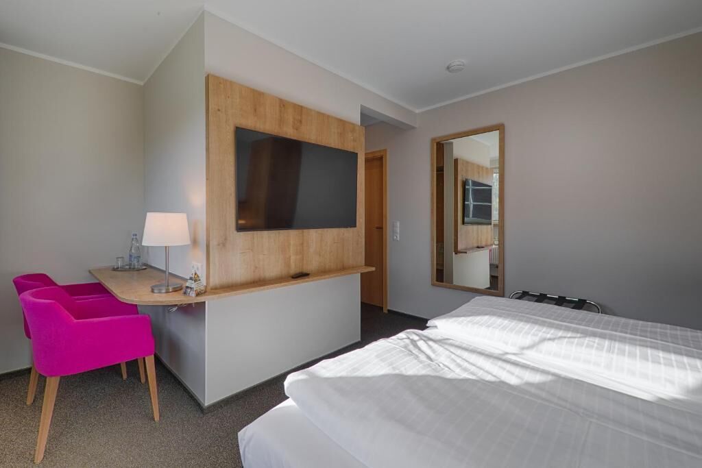 Ein Hotelzimmer mit einem Bett, einem Schreibtisch mit Stuhl, einem Fernseher und einem Spiegel.