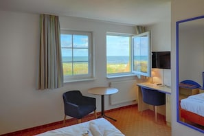 Habitación de hotel con cama, escritorio, silla, televisión y ventana con vista a la playa.