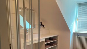 A modern bathroom with a glass shower enclosure, white cabinetry, and a wooden floor. - Elisabetha (Hannover)