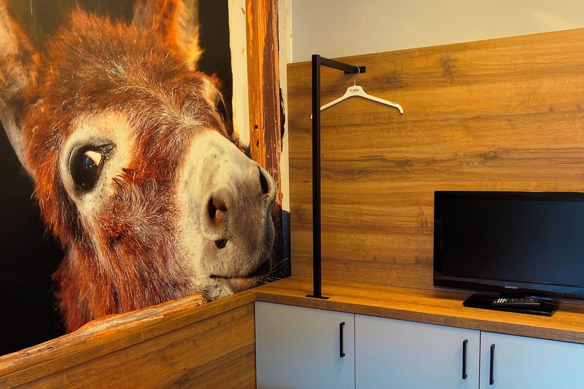 Una habitación con una cama, un televisor sobre un mueble de madera y un cuadro grande de un animal en la pared.