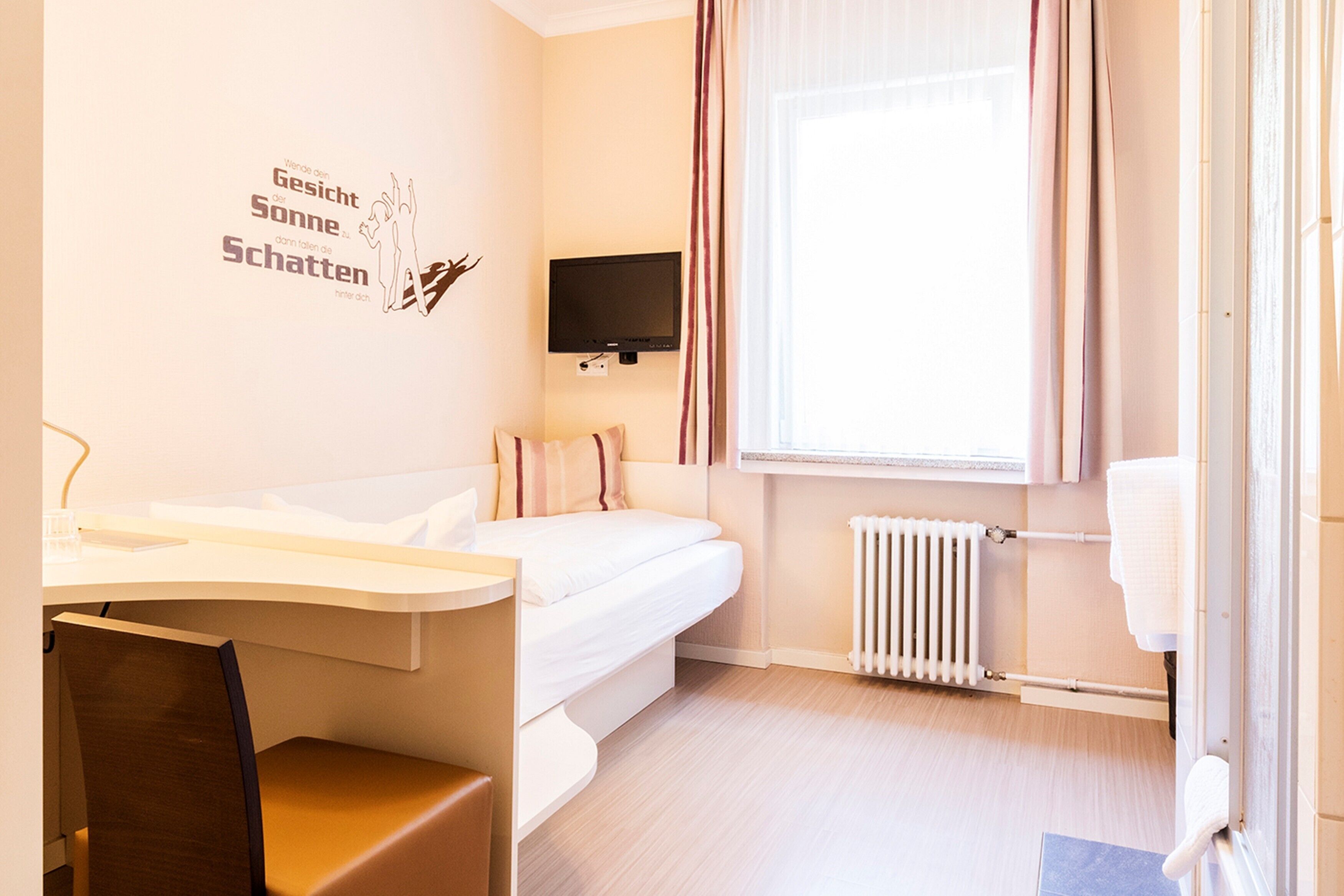Een hotelkamer met een bed, bureau, stoel, televisie, raam met gordijnen en een radiator.