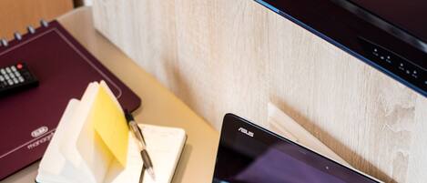 A laptop on a desk with a notebook, pen, and remote control.