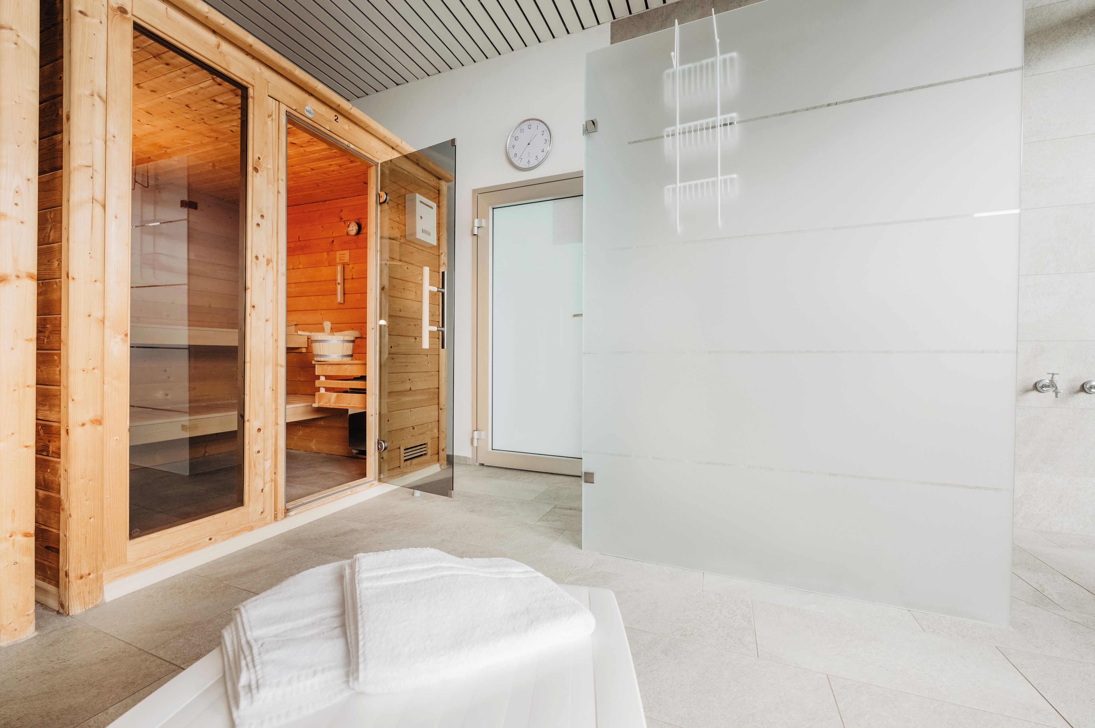 A modern spa room with a wooden sauna, a glass shower enclosure, and a white bathtub.