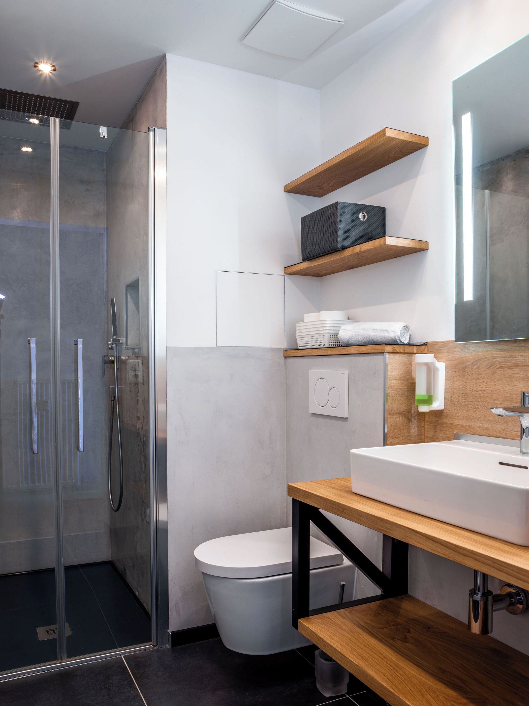 Et moderne badeværelse med en glasbrusekabine, et hvidt toilet og en trækommode med vask.