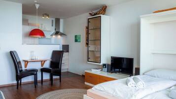Ein kleines Hotelzimmer mit Bett, Schreibtisch mit Stuhl, Fernseher und einer Minibar.