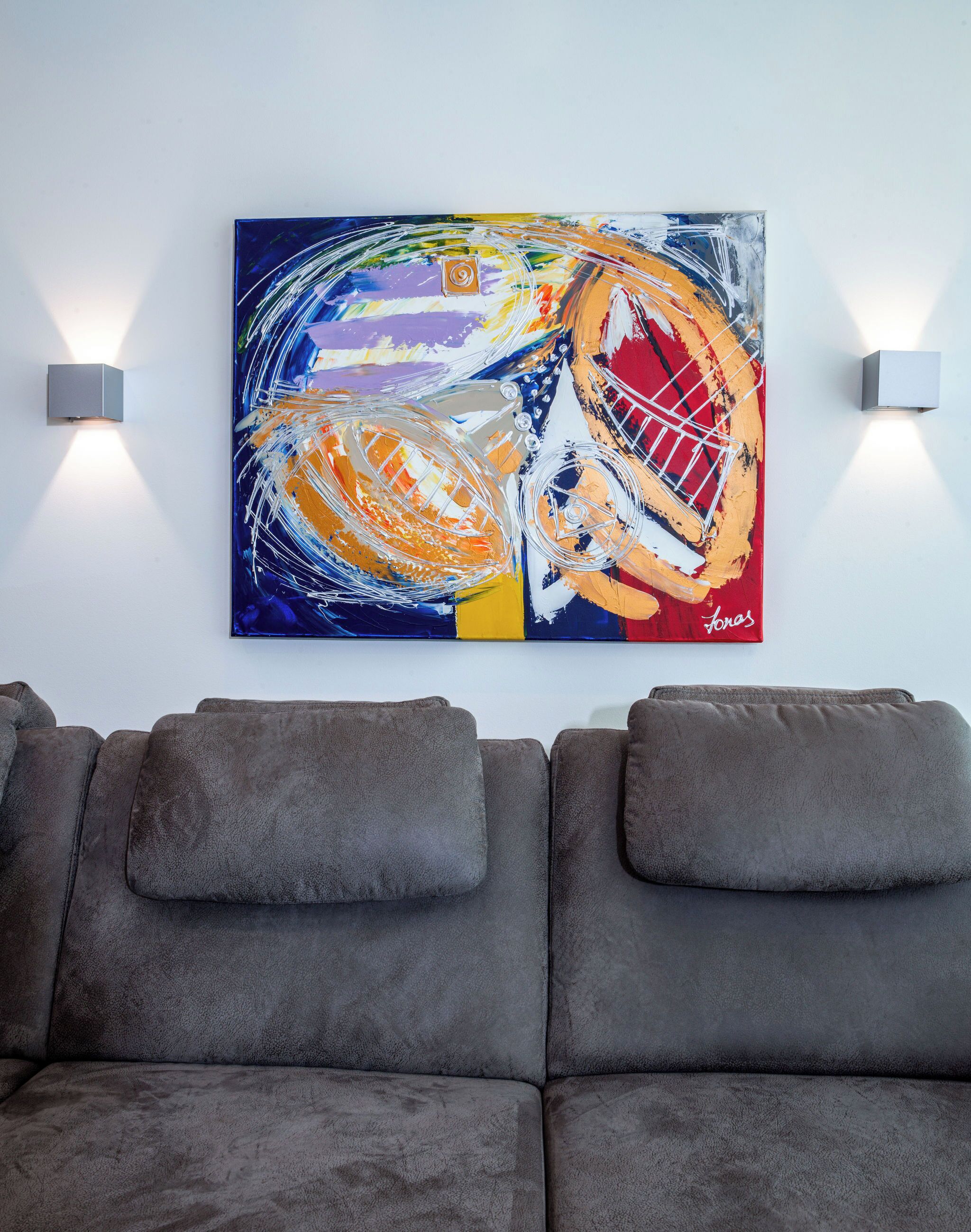 Een moderne woonkamer met een grijze bank en een kleurrijk abstract schilderij aan de muur.