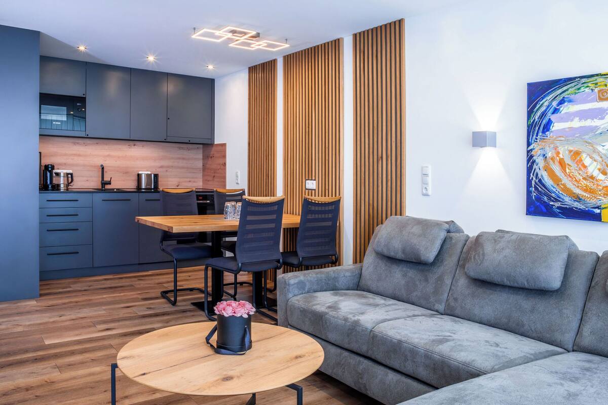 A modern living room with a grey sofa, wooden coffee table, and a dining area with a wooden table and chairs.