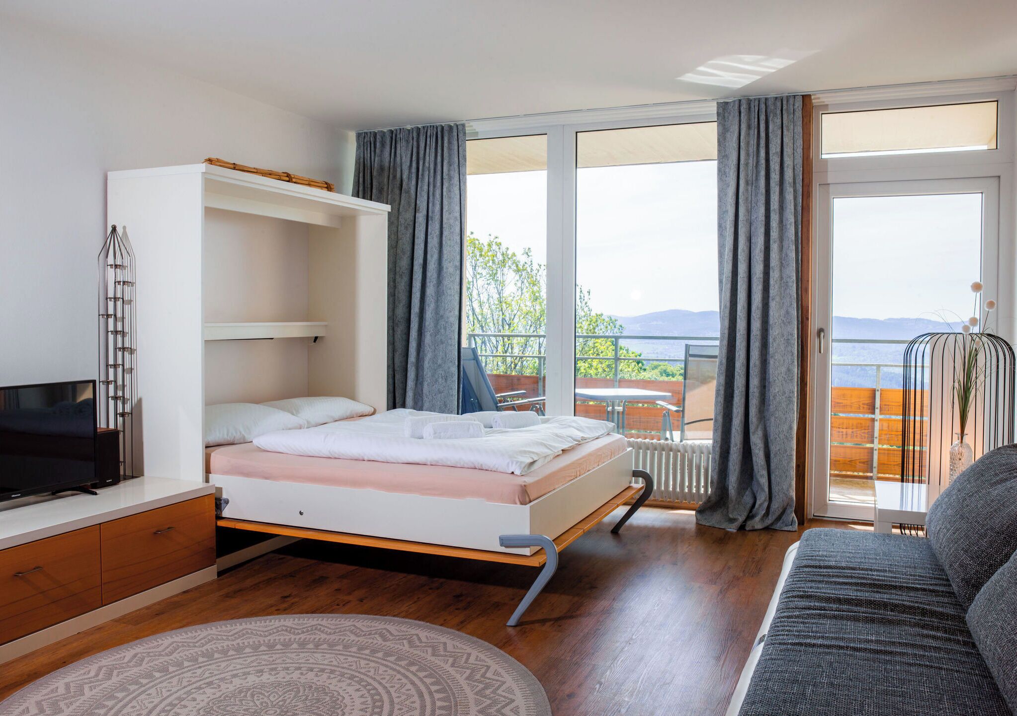 Un dormitorio con cama, televisión, sofá y balcón con vistas.