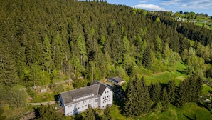 A large, multi-story building surrounded by dense forest, with a clear view of the surrounding landscape. - Greizer Kammhütte Gaststätte & Pension (Klingenthal)