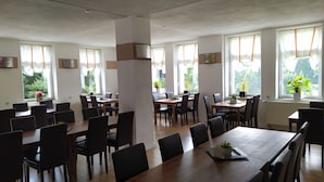 A spacious dining area with multiple tables and chairs, large windows with curtains, and potted plants. - Greizer Kammhütte Gaststätte & Pension (Klingenthal)