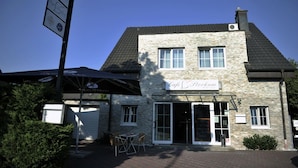A two-story stone building with a sign reading "Cafe Stockum." There are outdoor tables and chairs, and a covered area with umbrellas. - Hotel Villa Stockum (Düsseldorf)