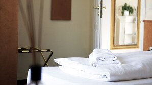 A hotel room with a neatly made bed, a hanging towel rack, and a mirror reflecting a bathroom with a sink and a plant. - Hotel Villa Stockum (Düsseldorf)