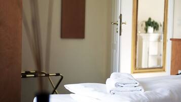 Ein Hotelzimmer mit einem ordentlich bezogenen Bett, einem Hängehandtuchhalter und einem Spiegel, der ein Badezimmer mit Waschbecken und Pflanze reflektiert.