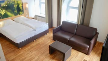 Une chambre d’hôtel avec un lit, un canapé en cuir marron, une petite table et de grandes fenêtres avec des rideaux.
