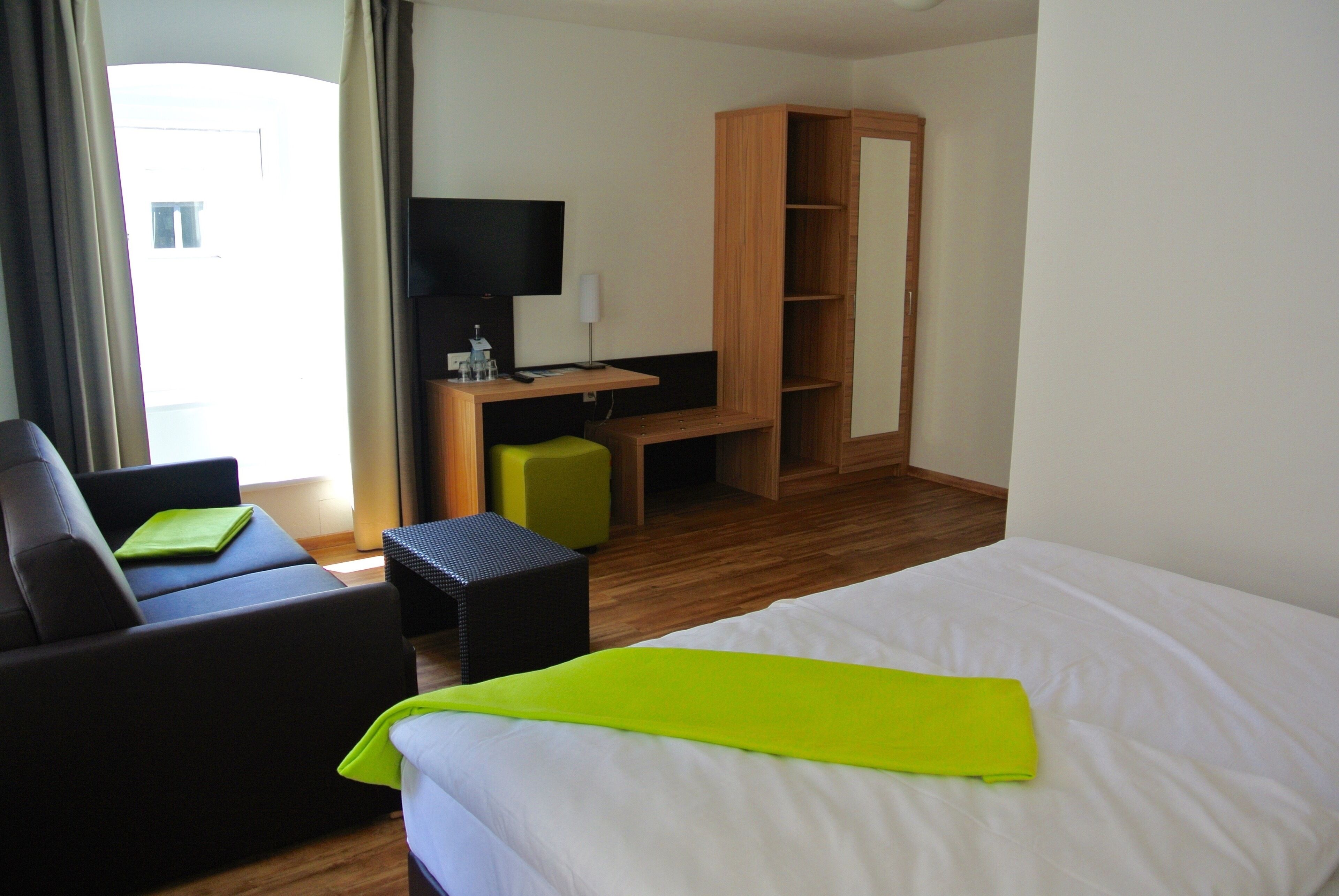A hotel room with a bed, a desk, a chair, a television, and a wardrobe.