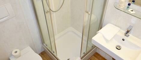 A modern bathroom with a glass-enclosed shower, a white sink with a mirror, and a toilet.