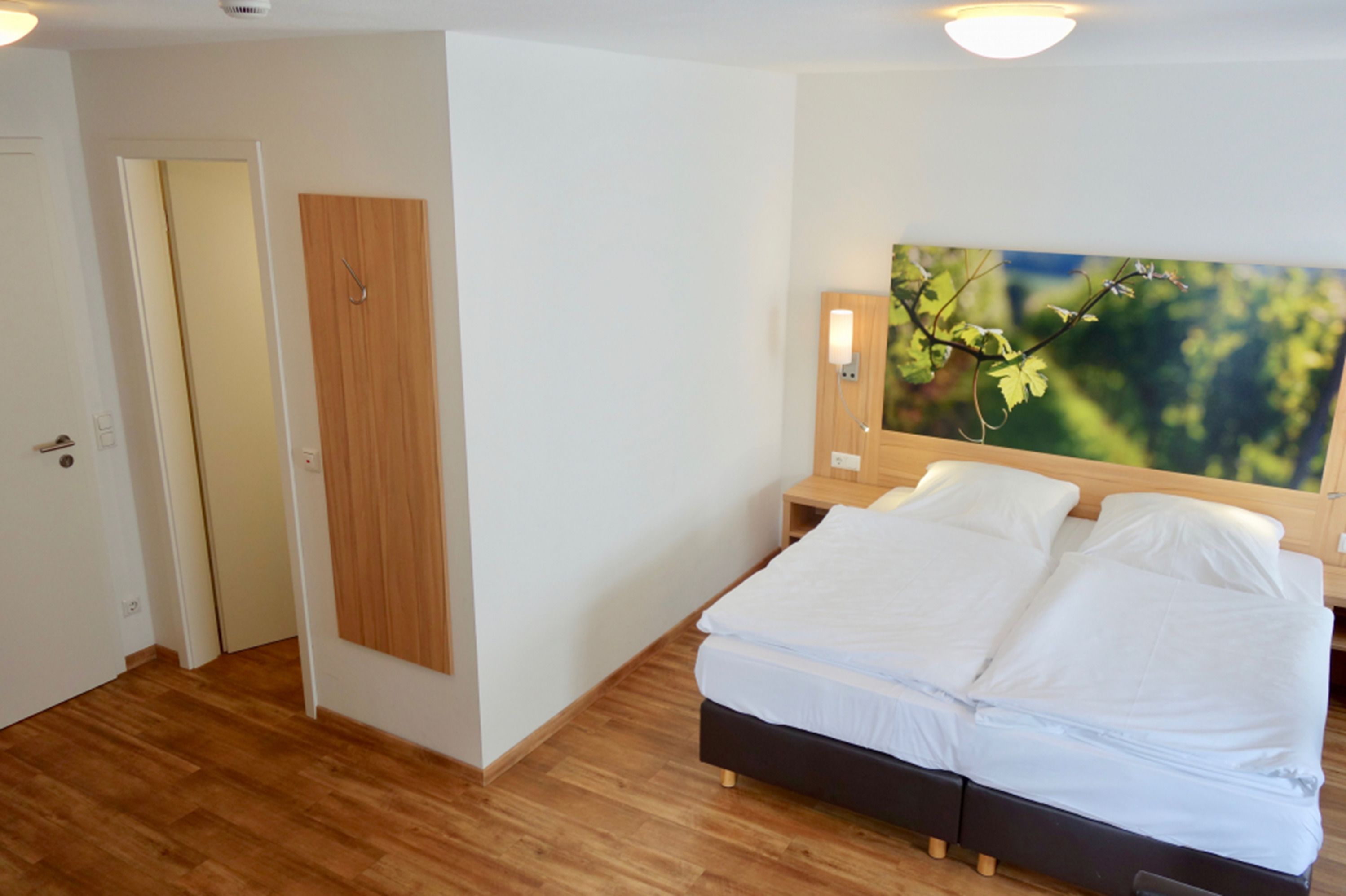 Un dormitorio con suelo de madera, una cama con ropa de cama blanca, un armario de madera y un televisor montado en la pared.
