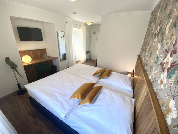 Een hotelkamer met een groot bed, een bureau met lamp, een televisie en een papegaai aan de muur.