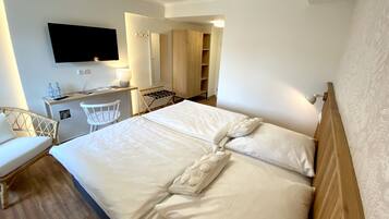 Quarto de hotel com uma cama grande, uma escrivaninha com cadeira, televisão fixada na parede e guarda-roupa de madeira.