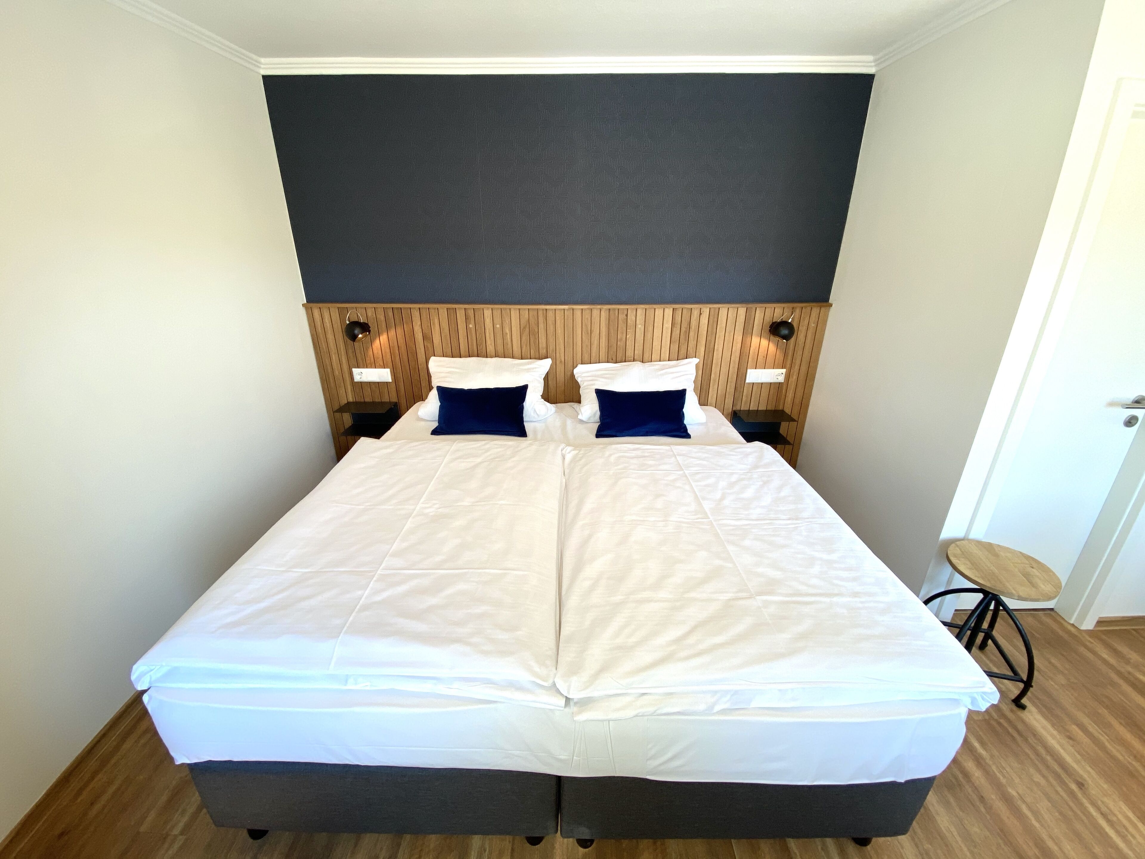 A double bed with white bedding, two blue pillows, and a wooden headboard. There are two bedside tables with lamps.