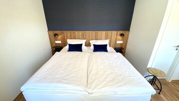 A double bed with white bedding, two blue pillows, and a wooden headboard. There are two bedside tables with lamps.