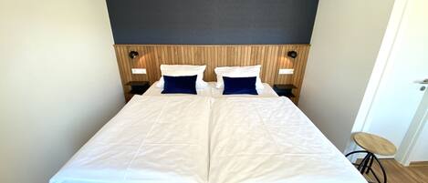 A double bed with white bedding, two blue pillows, and a wooden headboard. There are two bedside tables with lamps.