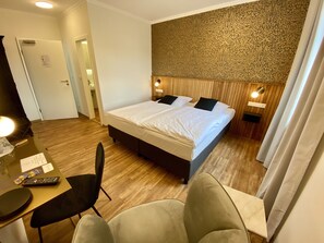 Ein Hotelzimmer mit einem Bett, Nachttischen, einem Schreibtisch mit Stuhl und einer Badezimmertür.