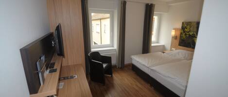 Habitación de hotel con escritorio de madera, una cama, una silla y un televisor.