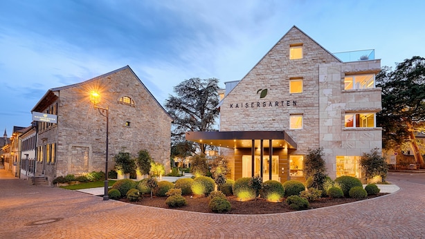 Un hôtel doté d’une façade en pierre, d’une entrée moderne et d’un aménagement paysager bien entretenu.