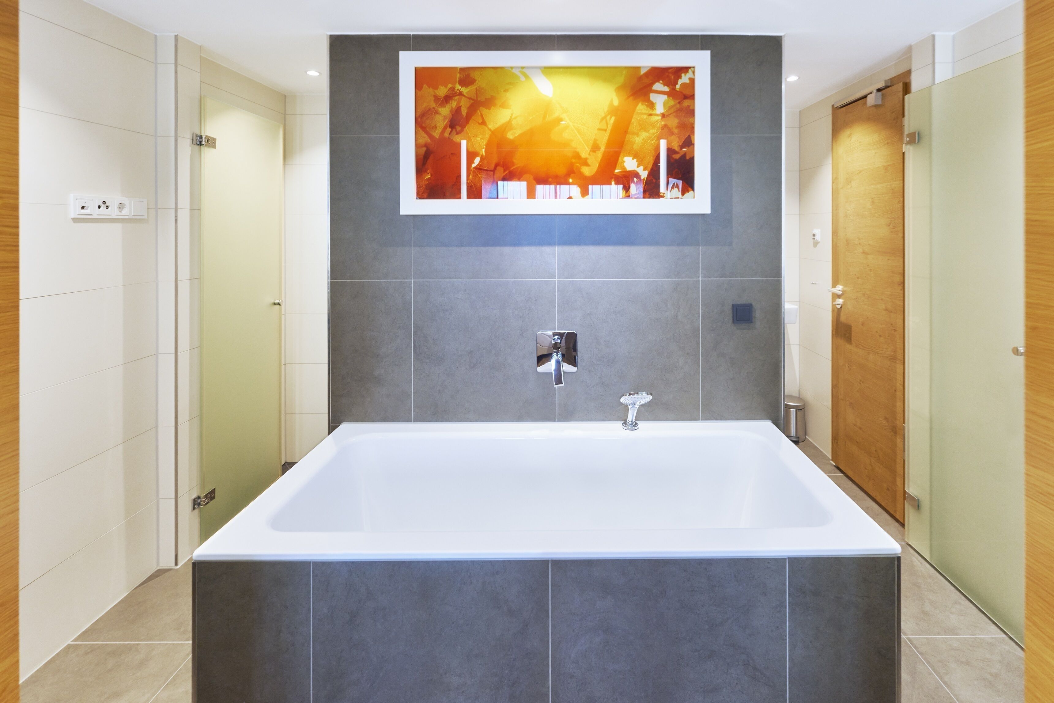 Une salle de bain moderne avec une grande baignoire, des carreaux gris et une œuvre d’art encadrée au-dessus de la baignoire.