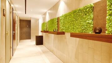 Un pasillo con pared verde, estantes de madera y un bote de basura.