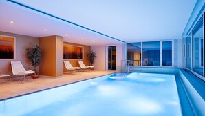 Un espace piscine intérieur moderne, doté de chaises longues et de plantes en pot.
