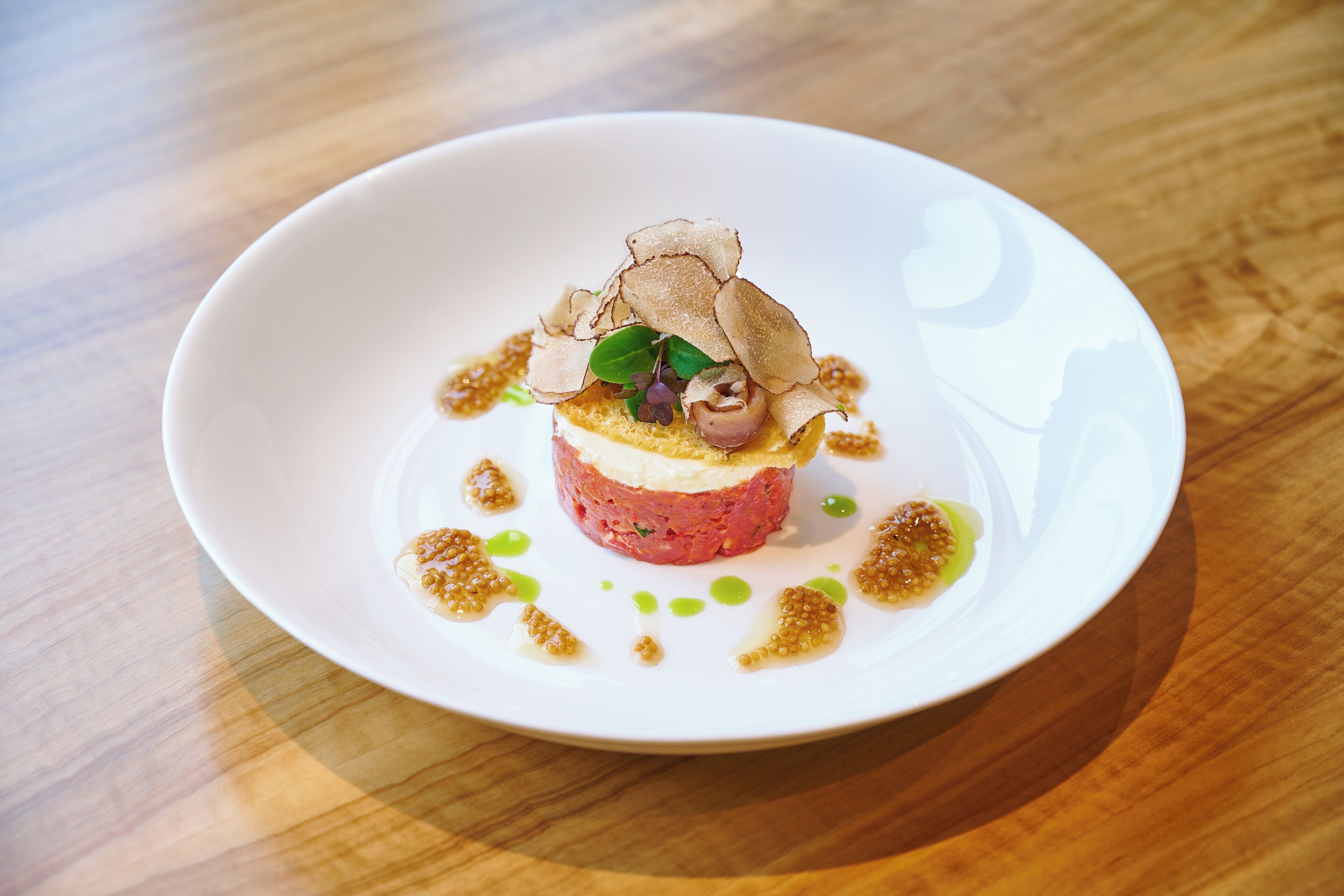 A white plate with a dish of food, garnished with leaves and edible flowers, on a wooden table.