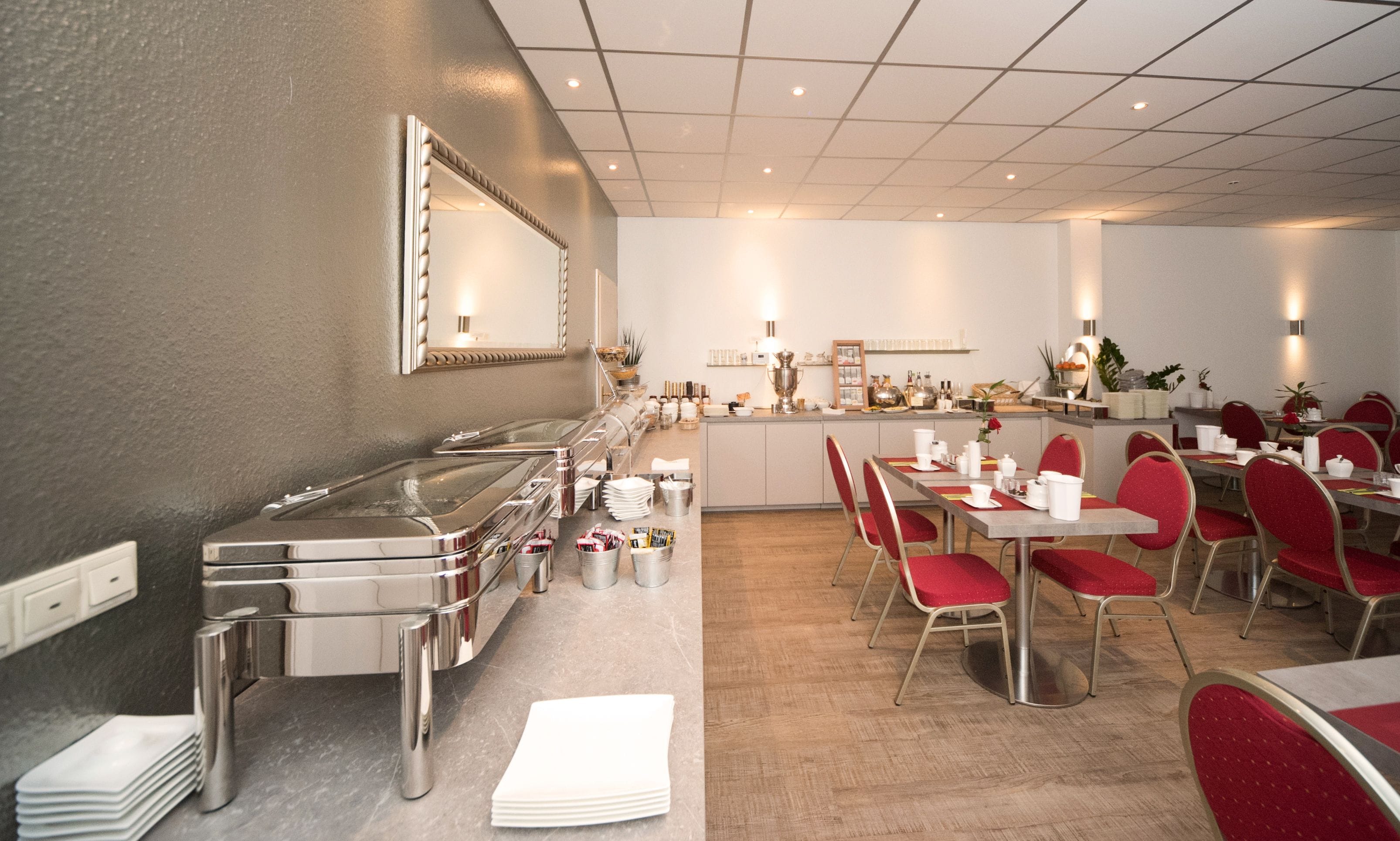 Un comedor moderno con una barra de buffet, una cocina al fondo y sillas tapizadas en rojo.