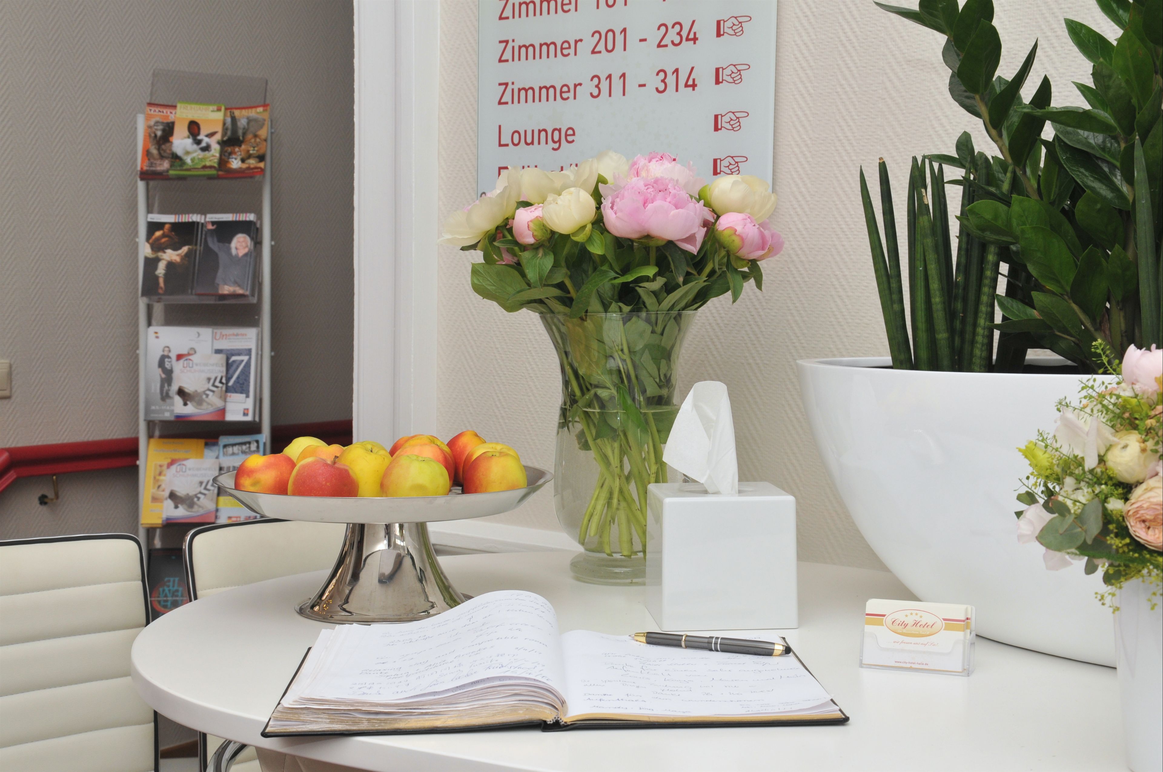 Una recepción de hotel con un jarrón de flores, un frutero, un bloc de notas y una tarjeta de presentación.