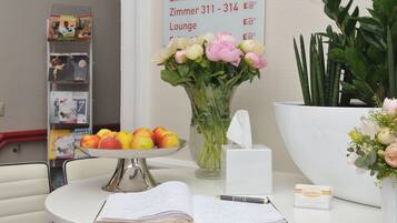 Una recepción de hotel con un jarrón de flores, un frutero, un bloc de notas y una tarjeta de presentación.