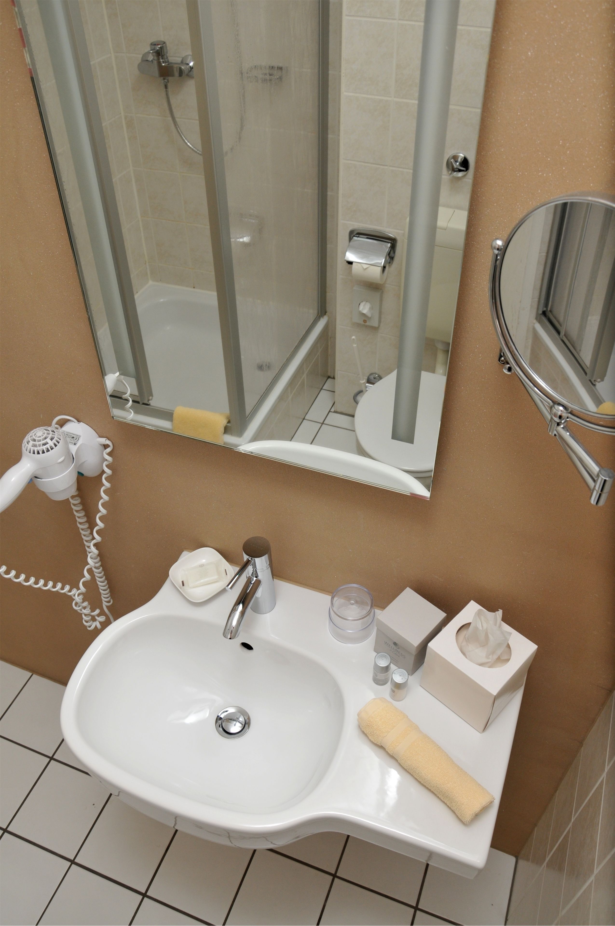 Ein Badezimmer mit einem weißen Waschbecken, einem Spiegel, einem Handtuch, einem Fön und einer Duschkabine.