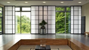 Una habitación amplia con piso de madera, una zona de estar central y ventanas grandes que ofrecen vista a la vegetación.