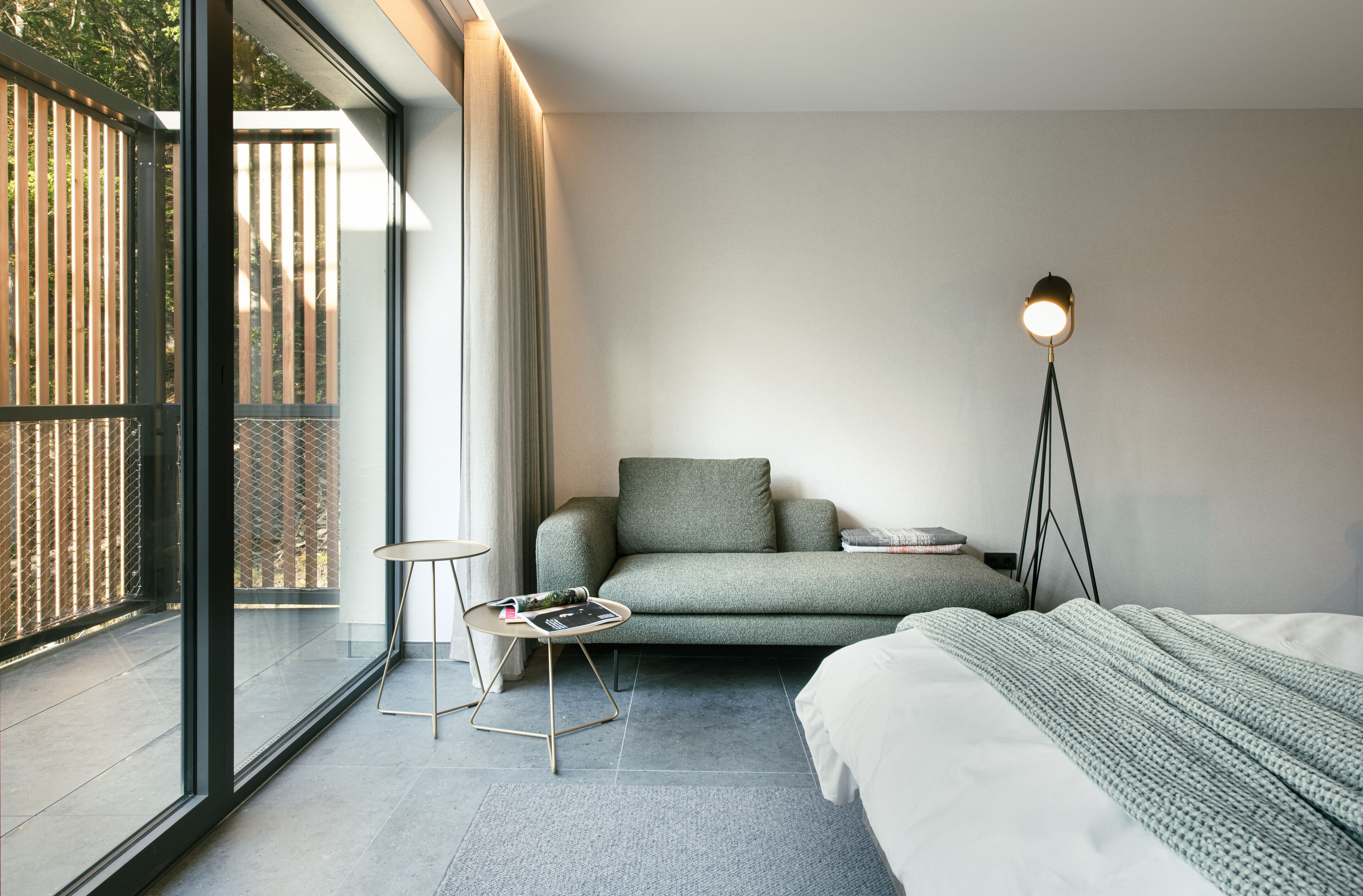 Ein modernes Schlafzimmer mit großem Fenster, einer Couch, einem Nachttisch und einer Stehlampe.