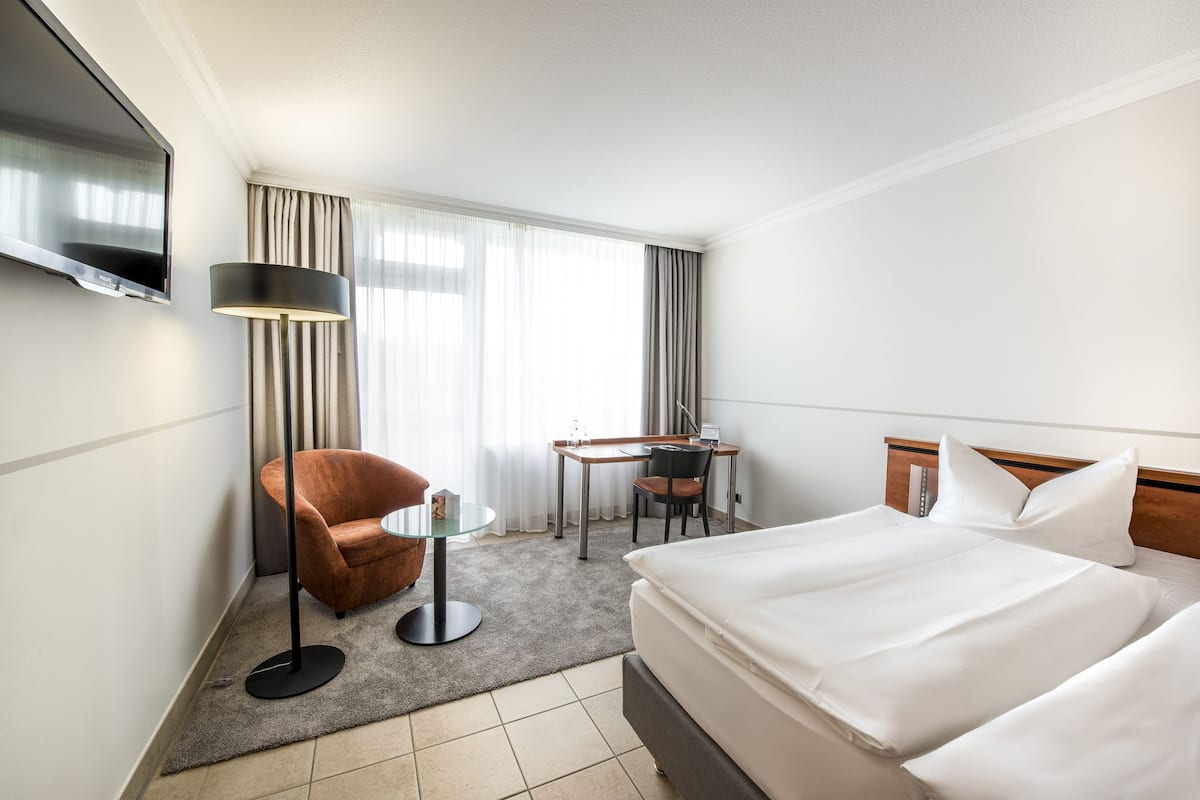 Una habitación de hotel con cama, escritorio, silla, televisor y lámpara.