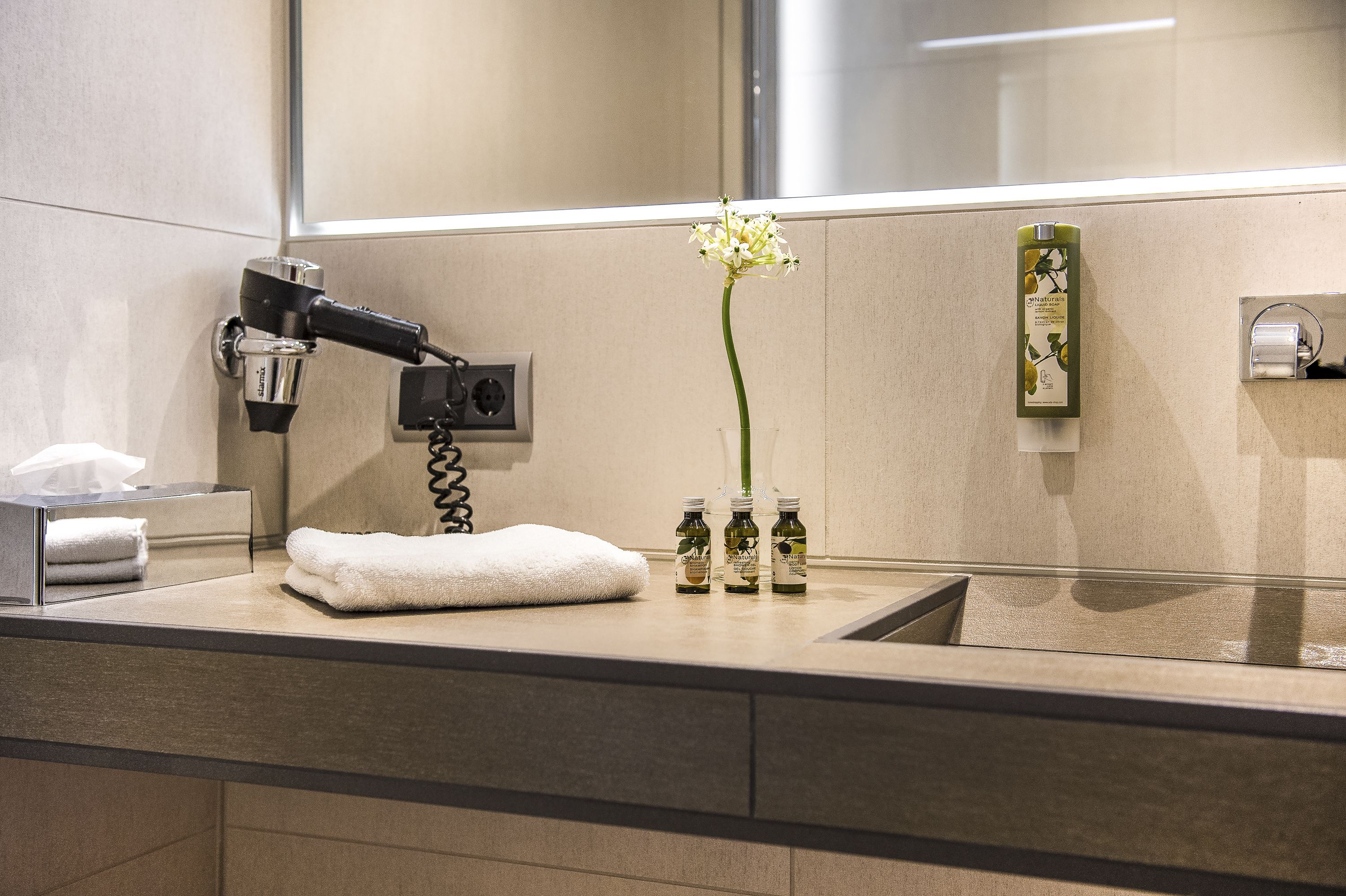 Une salle de bain avec un miroir, une serviette, une fleur et des articles de toilette.