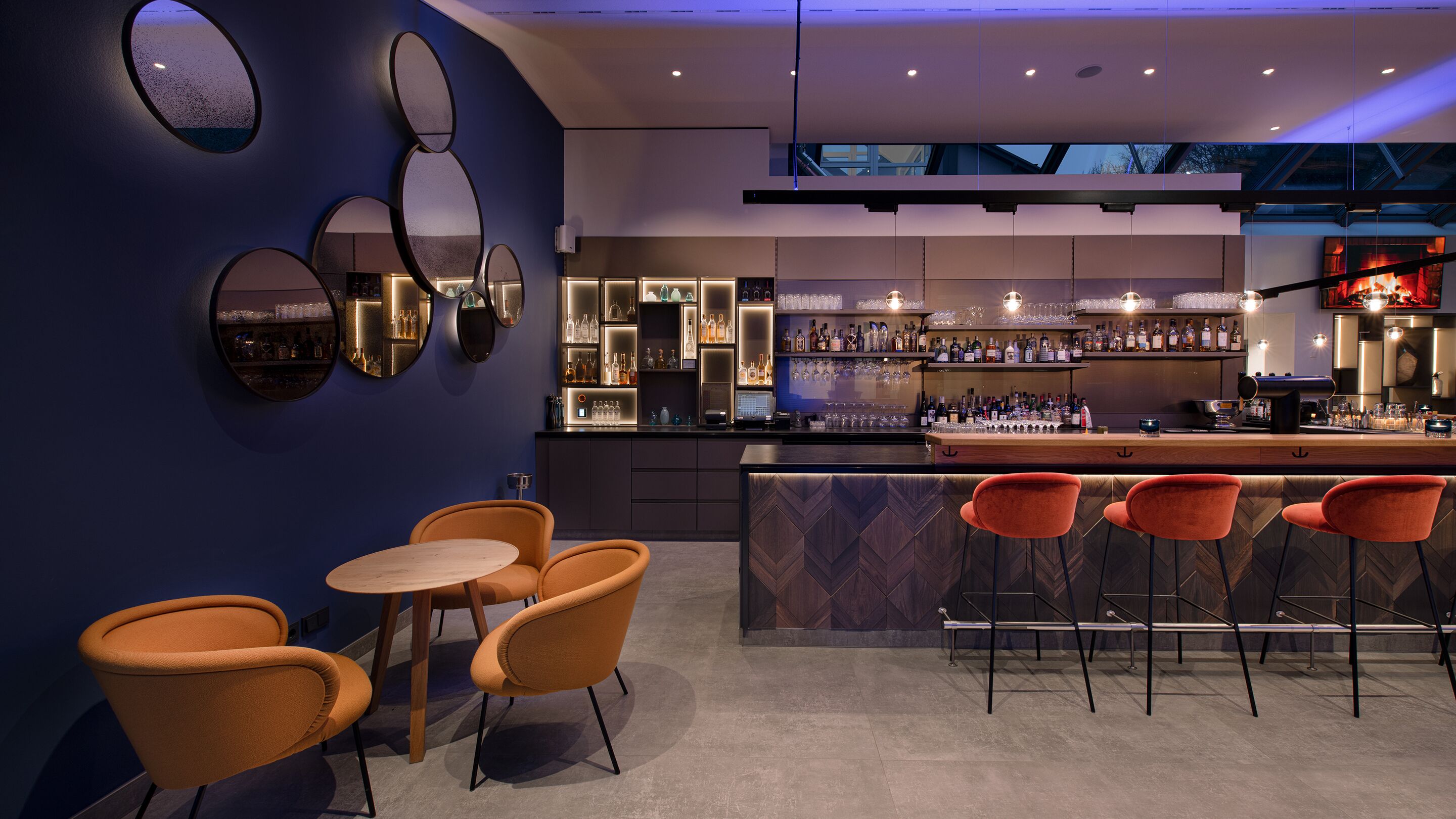 Eine moderne Bar mit einer Theke, Sitzgelegenheiten und einer Auswahl an Flaschen und Gläsern.